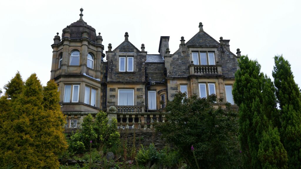 Charming stone manor house with tower surrounded by lush gardens and trees.