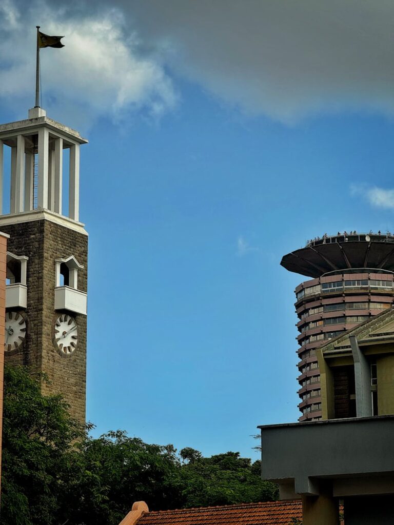 Skyline view of Nairobi with KICC and a historic clock tower under a blue sky.